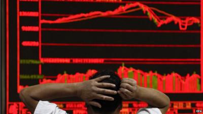 Man with his hands on his head watching falling market figures (in red) on a large screen