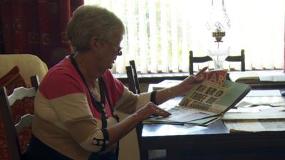 Joy Bingham reads a newspaper report about the deaths of her father, her sister and her sister