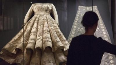 A member of Buckingham Palace staff stands next to a glass case containing Queen Elizabeth IIs wedding dress