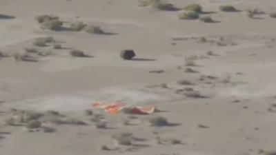 Capsule on desert floor with brightly coloured parachute underneath it