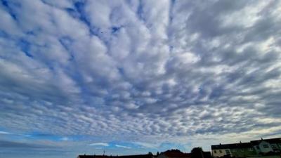 Patchy cloud over a field with some houses along the parameter.