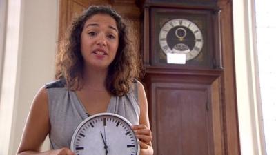 BBC Mundo journalist Gabriela Torres holding a clock, standing in front of a clock