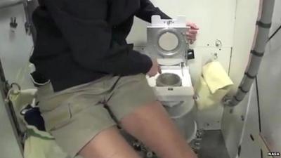 astronaut points at space toilet bowl