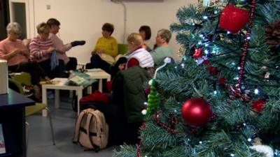 A group of women knit next to a Christmas tree