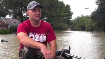 Man sat on a boat with water and trees behind him