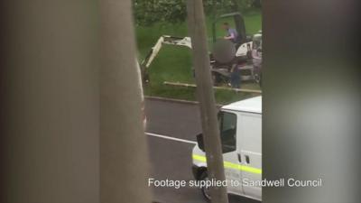 A digger breaking through a fence