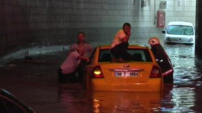 A man sits on his car roof as emergency services push it