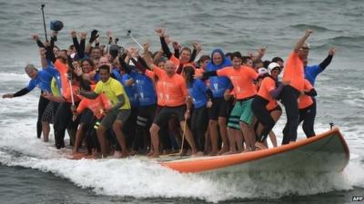 Sixty-six surfers from Huntington Beach ride the world's largest surfboard