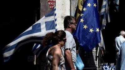 People walk past Greek and WU flags in Athens