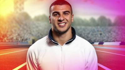 Adam Gemili smiles with a long racing track and a crowd behind him.