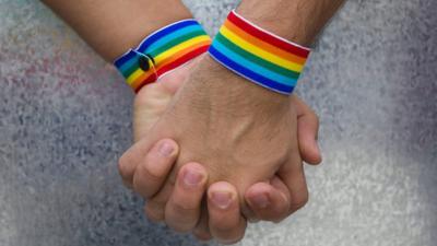 Two people holding hands with rainbow bracelets