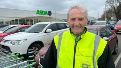 Lloyd is smiling in a high-vis jacket outside the ASDA supermarket