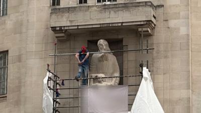 man in Spiderman mask hanging off of scaffolding