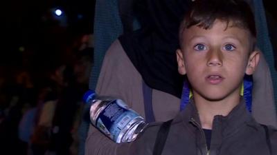 Close up of a boy looking straight ahead as he prepares to board a ferry from the Greek island of Lesbos to the mainland