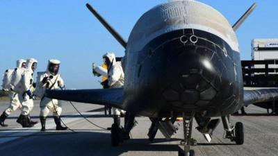 People in special suits work near the X-37B