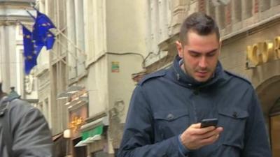 Man walking looking at mobile phone, EU flags in background