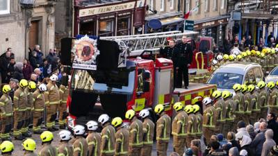 Firefighters line the streets as a coffin passes by