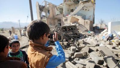 A boy uses a cell phone to take photos of the wreckage of a house destroyed by a Saudi-led air strike on the outskirts of Sanaa, Yemen