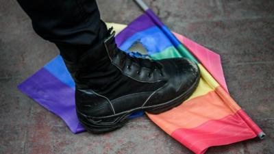 A big blag boot stamping down on a ripped rainbow flag