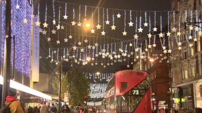 A red bus passes underneath starry lights criss-crossing above Oxford Street.