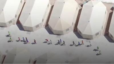 Aerial footage showing a line of children walkign through the camp