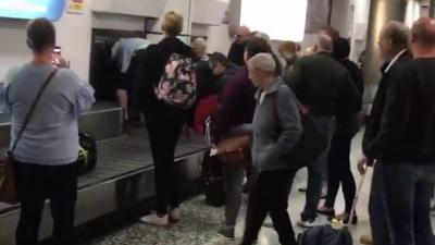 A passenger pulls bags through a carousel hatch.