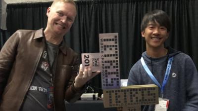 An older man holds a Tetris shaped trophy along with a younger teenage boy