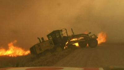 Road grader surrounded by fire