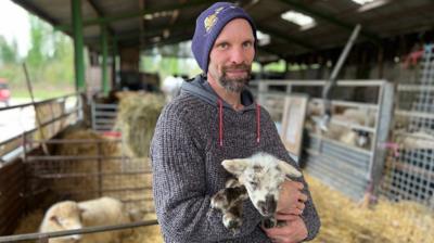 A shepherd holds a lamb