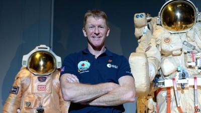 Tim Peake poses beside spacesuits as he talks to reporters at the Science Museum, London