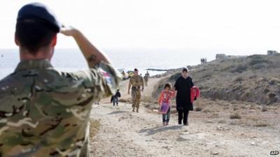 British Military personnel escort migrants who arrived by boat away from the shore