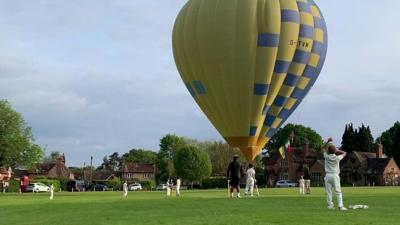 A hot air balloon lands on a cricket field