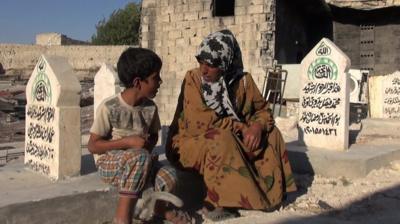 Aisha Ali and Ahmed Mohammed Bitar sit in the cemetery.