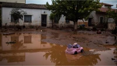 A toy car is seen in a flooded street next to a damaged house in the town of Mandra