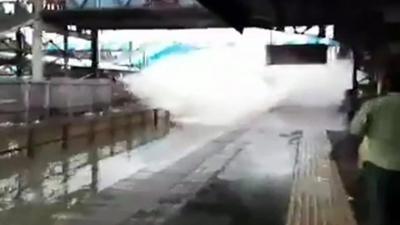 A train in Mumbia speeding though a flooded platform.