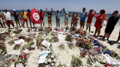 People on beach hold hands around floral tributes