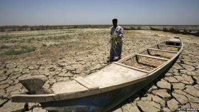 An Iraqi man walks past a canoe sitting on dry, cracked earth in the Chibayish marshes near the southern Iraqi city of Nasiriyah