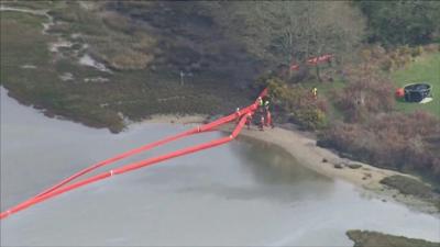 Workers and a boom in the water at Poole Harbour