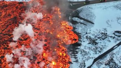 Bright orange lava flow moves across road in snowy landscape