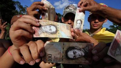 People hold up the 100-bolivar note