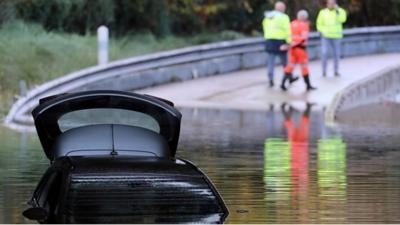 Rescuers walk by a car partially submerged in the water on a flooded road of Mandelieu-la-Napoule