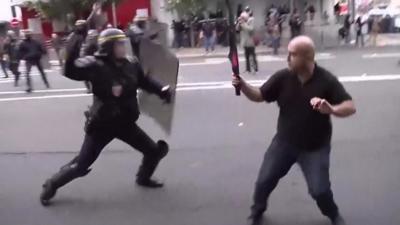 A police officer and protester both hold up sticks as they clash