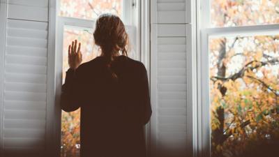 Young woman looks out of a white shuttered window