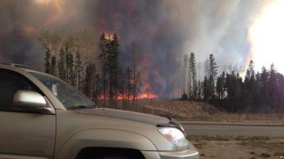 A car is parked with fires raging in the distance in Alberta, Canada.