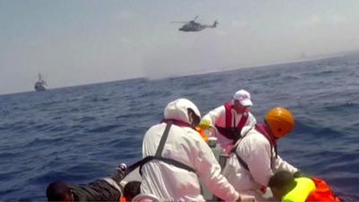 Rescuers searching for hundreds of migrants in the Mediterranean help a man out of the water