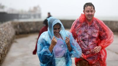 People walk in the rain along the sea wall next to the Palace Pier in Brighton, southern England on 5 August 2023