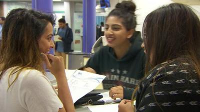 Three seated students with A-Level results in hand