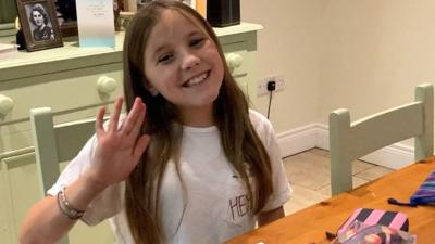 a-young-girl-called-daisy-sits-at-a-kitchen-table-and-waves