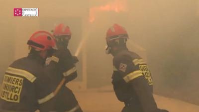 Three firefighters shooting a hose of water at some flames.