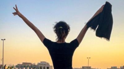 Woman protester in Iran holding headscarf with arms raised